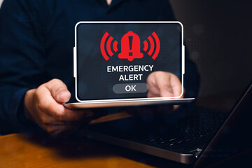 A person holds a laptop displaying a red emergency alert notification with an exclamation mark and...