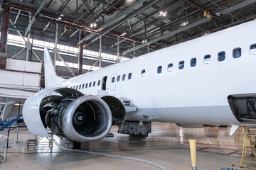 White passenger airliner in the airplane hangar. Aircraft under maintenance. Checking mechanical systems for flight operations