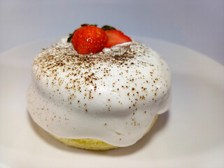 A round light-colored fluffy cake topped with whipped cream and garnished with fresh strawberries...