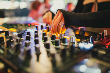 DJ adjusting knobs on professional audio mixer at live music event with vibrant lights, capturing...