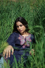 A Kashmiri girl in a traditional blue kurta stands amid spring’s wilderness — framed by blue...