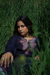 A Kashmiri girl in a traditional blue kurta stands amid spring’s wilderness — framed by blue...