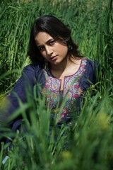 A Kashmiri girl in a traditional blue kurta stands amid spring’s wilderness — framed by blue...