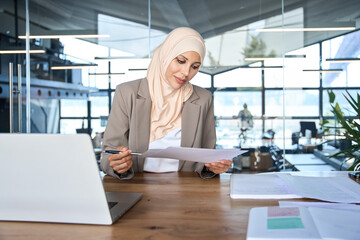 Focused Indian or arabian businesswoman working in office. Copy space. Middle eastern muslim woman in hijab using laptop computer for business analysing, trading, banking, financial data or insurance