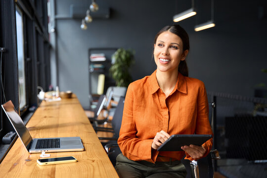 Executive CEO businesswoman professional holding digital tablet pc device for work in office, looking dreaming at copy space. Successful latin hispanic young woman using pad computer for business app