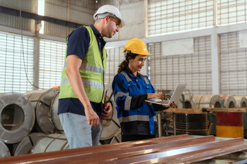 Two workers collaborate in a warehouse while examining data on a laptop during the day