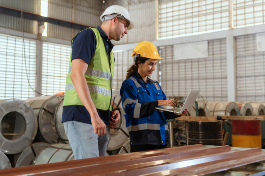 Two workers collaborate in a warehouse while examining data on a laptop during the day