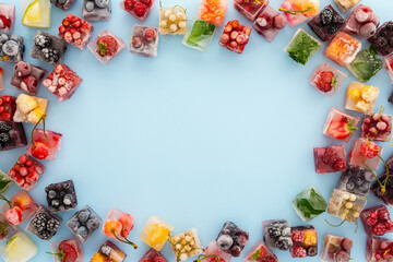 Frame of ice cubes with frozen berries and fruits and mint on blue background