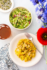 Stewed rice with chicken breast and mixed salad with radishes and various seeds, a served table with food and a vase of flowers