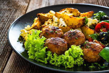 Greek style fried meatballs, fried potato wedges with feta cheese and tomato salad on wooden table	