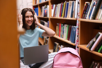 Student with laptop and backpack between shelves in library