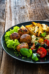 Greek style fried meatballs, fried potato wedges with feta cheese and tomato salad on wooden table	