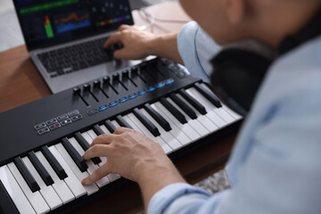 Man working with MIDI keyboard and laptop at table indoors, selective focus