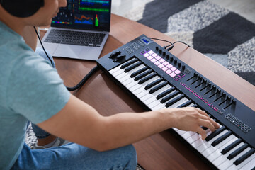Man working with MIDI keyboard and laptop at table indoors, closeup