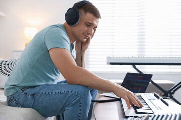 Man in headphones working with MIDI keyboard at table indoors