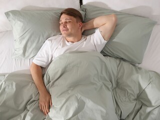 Young man sleeping on bed with soft mattress at home, top view