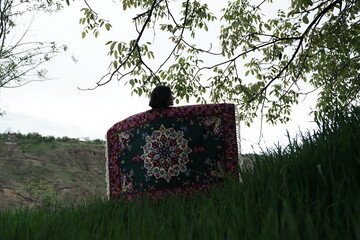 A young girl in an open field showcasing a beautifully handcrafted Kashmiri carpet, highlighting...