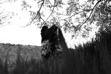Black and white photograph of a girl holding an abstract-patterned carpet in wide open fields,...