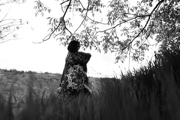 Black and white photograph of a girl holding an abstract-patterned carpet in wide open fields,...