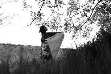 Black and white photograph of a girl holding an abstract-patterned carpet in wide open fields,...