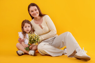 Mother and her little daughter with bouquet of beautiful chamomile flowers on orange background