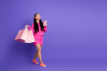 Young woman enjoying shopping holding bags and smartphone, dressed in vibrant pink clothing against...