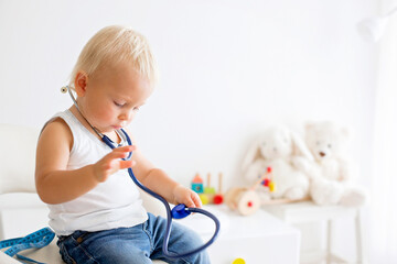Sweet child, baby boy, playing doctor using stethoscope to listenhis hearth beat