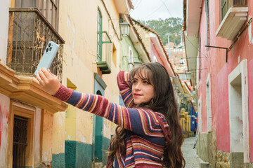 woman in casual clothes walking in jaen street in the city of la paz and taking a selfie with her...