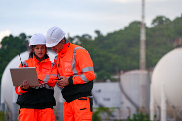 Two engineers in high-visibility safety gear and hard hats discuss project plans on a laptop in...