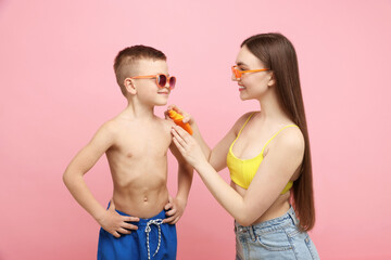 Mother applying sun protection cream onto her son's skin on pink background