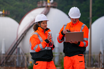 Two engineers in high-visibility safety gear and hard hats discuss project plans on a laptop in...