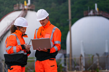 Two engineers in high-visibility safety gear and hard hats discuss project plans on a laptop in...