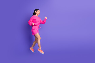 Young woman in pink attire joyfully walking on a vibrant purple background, expressing energy and...