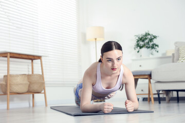 Young woman in sportswear doing plank exercise at home. Space for text