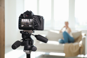 Woman on sofa in studio, focus on video camera recording her