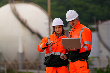 Two engineers in high-visibility safety gear and hard hats discuss project plans on a laptop in...