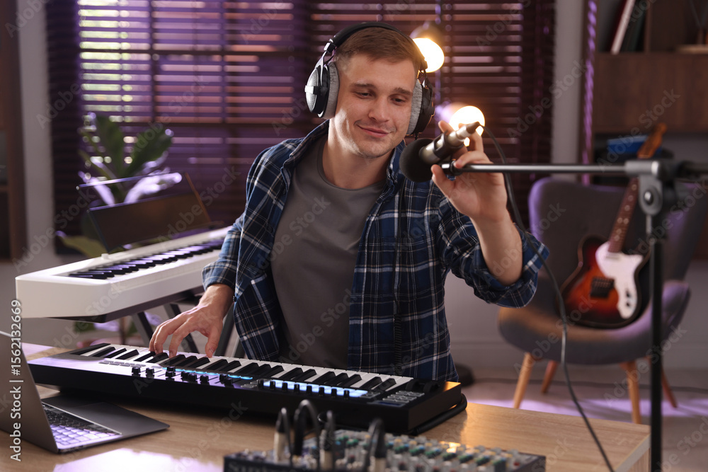 Poster man in headphones working with midi keyboard and microphone at table in home studio