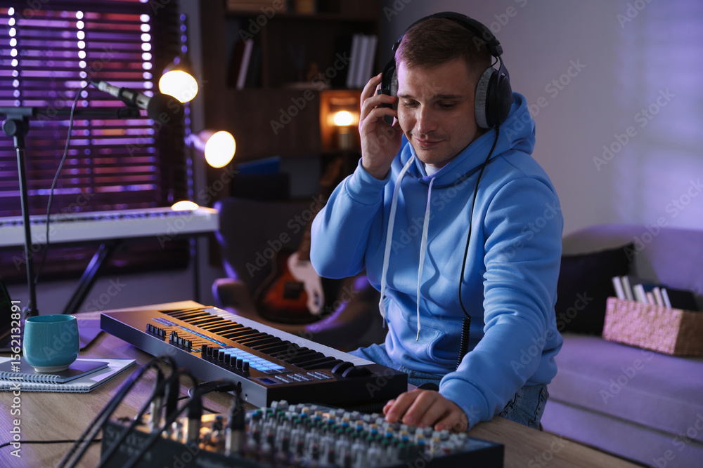 Poster man in headphones working with midi keyboard and dj mixer at table in home studio