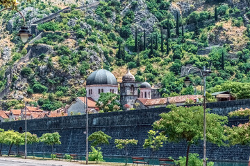 Ancient stone walls and dome of the Serbian Orthodox Church of St. Nicholas in Kotor, Montenegro, set on a backdrop of rugged mountains. Scene showcases the rich history and scenic beauty of Kotor