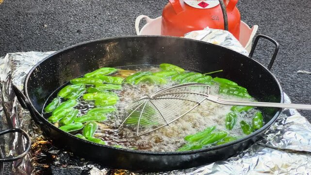 Small green peppers are cooked in oil in a large pot at a food fair. Pimientos del Padron, a variety of pepper native to Galicia. Concept of snacks of Spain. High quality 4k footage