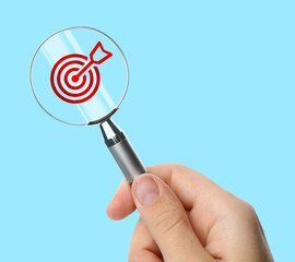 Targeting. Woman holding magnifying glass with bullseye icon inside against light blue background,...