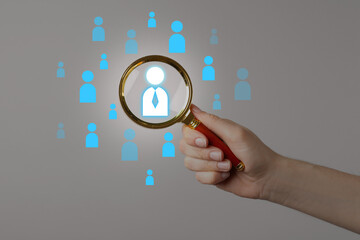 Targeting. Woman holding magnifying glass over human icons against light grey background, closeup