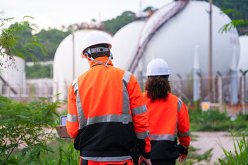 Two engineers in high-visibility safety gear and hard hats discuss project plans on a laptop in...