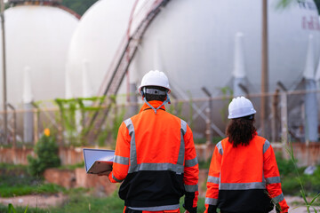 Two engineers in high-visibility safety gear and hard hats discuss project plans on a laptop in...