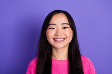 Cheerful young woman in a pink sweater with vibrant makeup against a purple backdrop exuding...