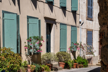 Building with green shutters and a flower garden in front. The shutters are open. There are potted plants in front of building