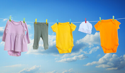 Different baby clothes drying on washing line against blue sky