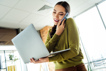 Young professional woman multitasking with laptop and phone in a modern office while staying...