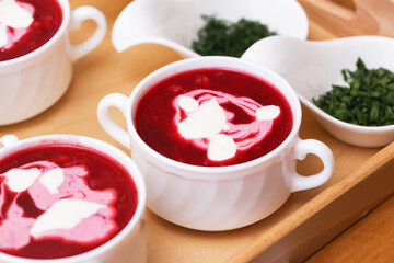 Hot beetroot soup with sour cream. Traditional red borscht served in white bowls. Fresh herbs on the side. Classic Eastern European cuisine. Delicious vegetarian dish. Comfort food for winter.