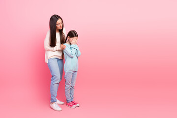 Mother consoles her young daughter in a close bonding moment against a pink background showing love and comfort
